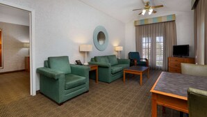 A hotel room with a green sofa set, a wooden coffee table, a TV, and a ceiling fan. - La Quinta Inn Tampa Airport Stadium Westshore (Tampa)