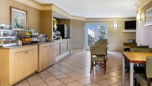 A hotel dining area with a buffet counter, seating, and a television. - La Quinta Inn Tampa Airport Stadium Westshore (Tampa)