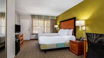 Hotelkamer met een bed, een bureau met lamp, een televisie en een kleine koelkast.
