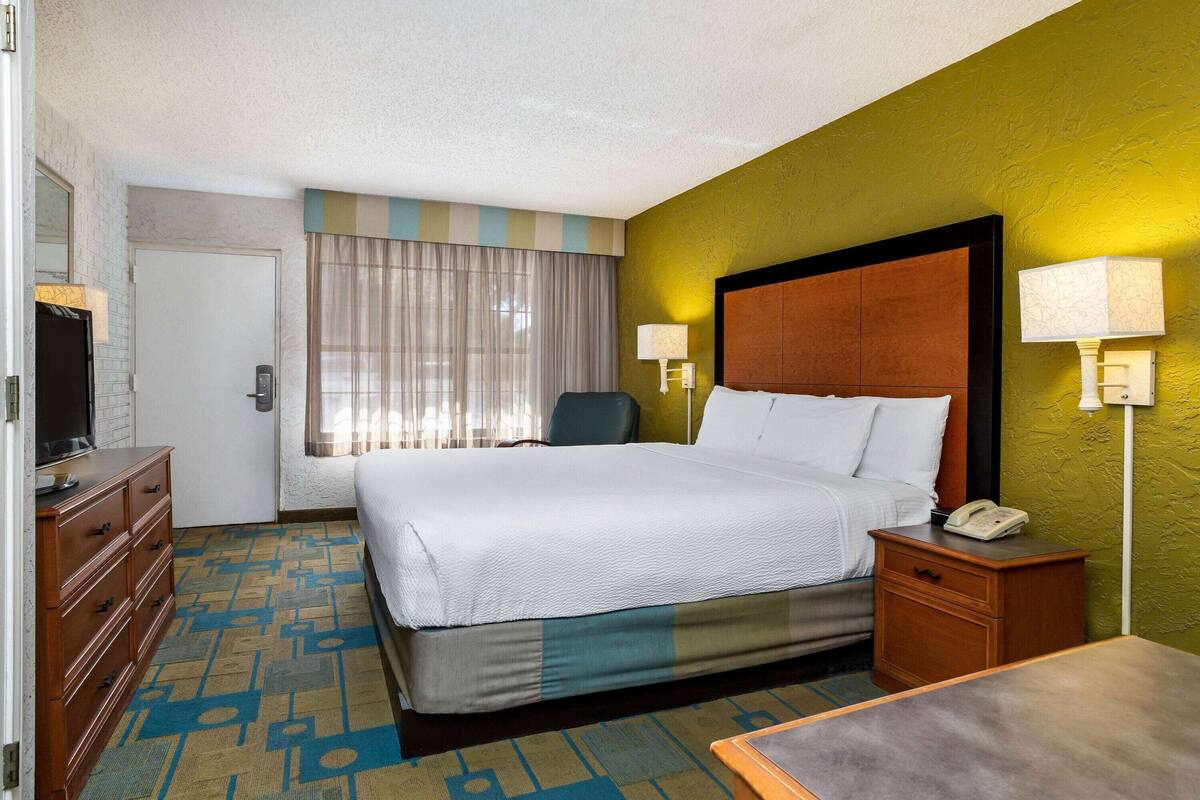 Una habitación de hotel con cama, escritorio, silla, cómoda y televisor.