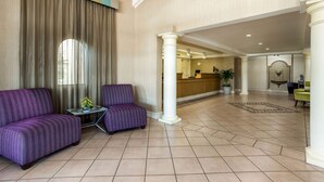 A lobby with a reception desk, two purple armchairs, a small table with a plant, and a large column. - La Quinta Inn Tampa Airport Stadium Westshore (Tampa)