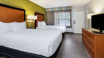 A hotel room with two beds, a TV, a dresser, and a window with curtains.