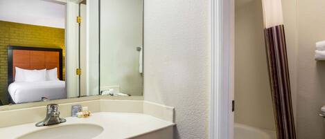 A bathroom with a white sink, a mirror, a shower curtain, and a visible toilet.