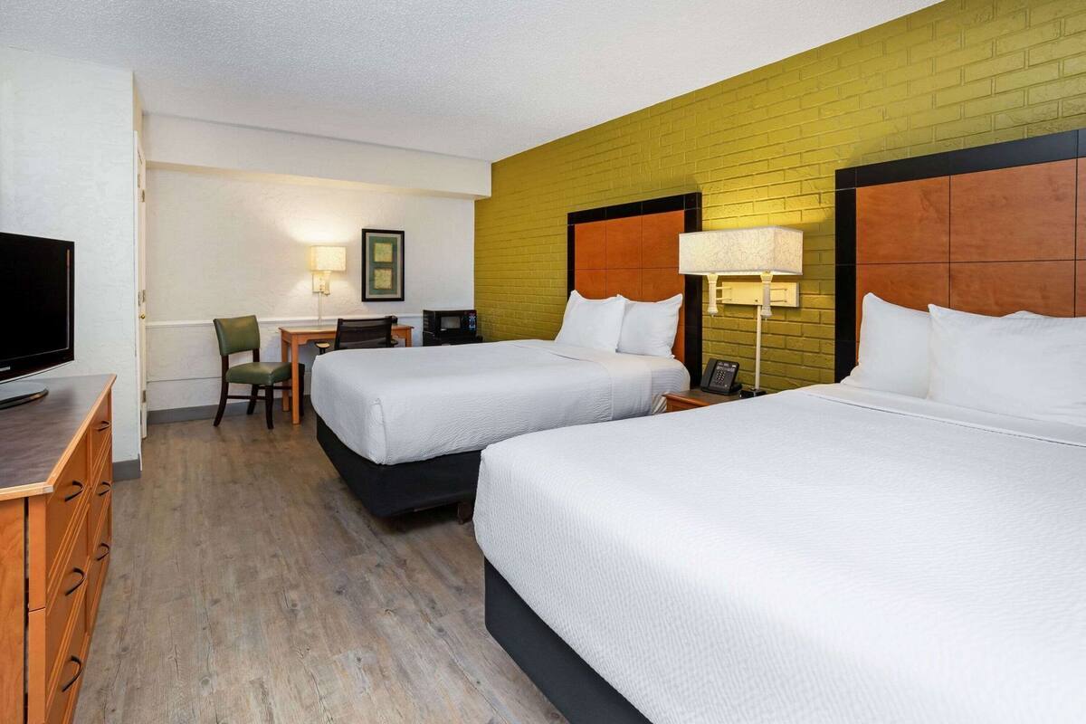 Habitación de hotel con dos camas, un escritorio, una silla, un televisor y una lámpara.