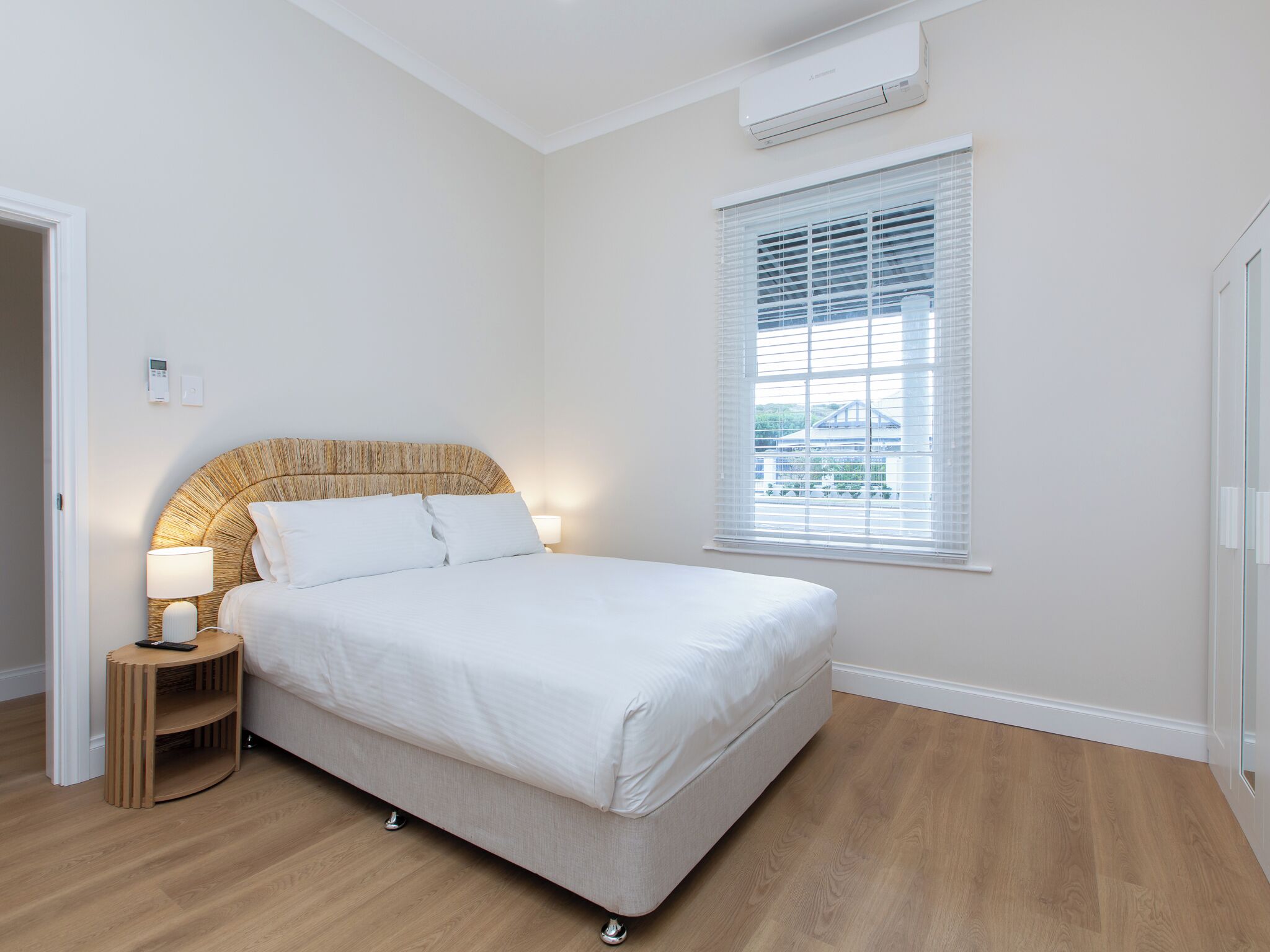 A bedroom with a bed, bedside table, lamp, and window with blinds.