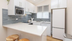 Una cocina moderna con armarios blancos, salpicadero gris, microondas empotrado, un lavamanos y un refrigerador.
