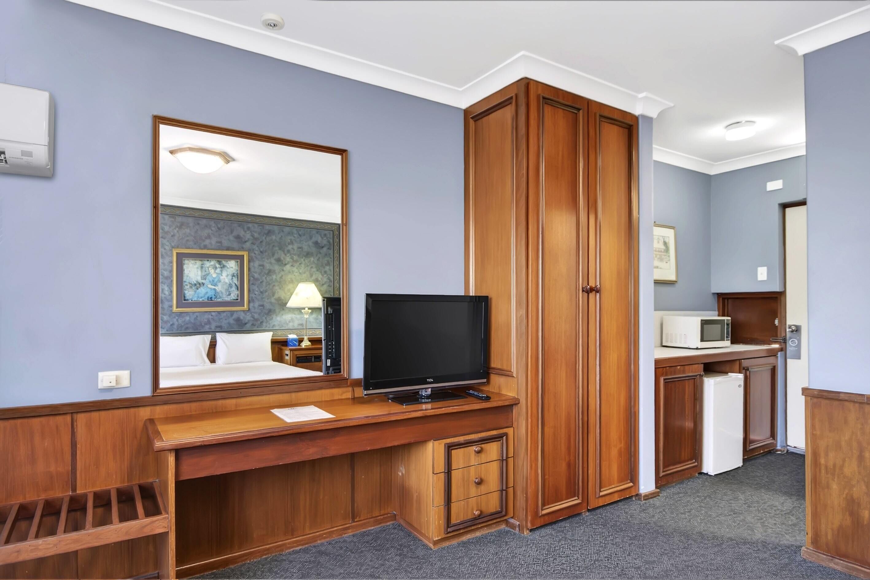 Una habitación de hotel con escritorio de madera, televisor y kitchenette.