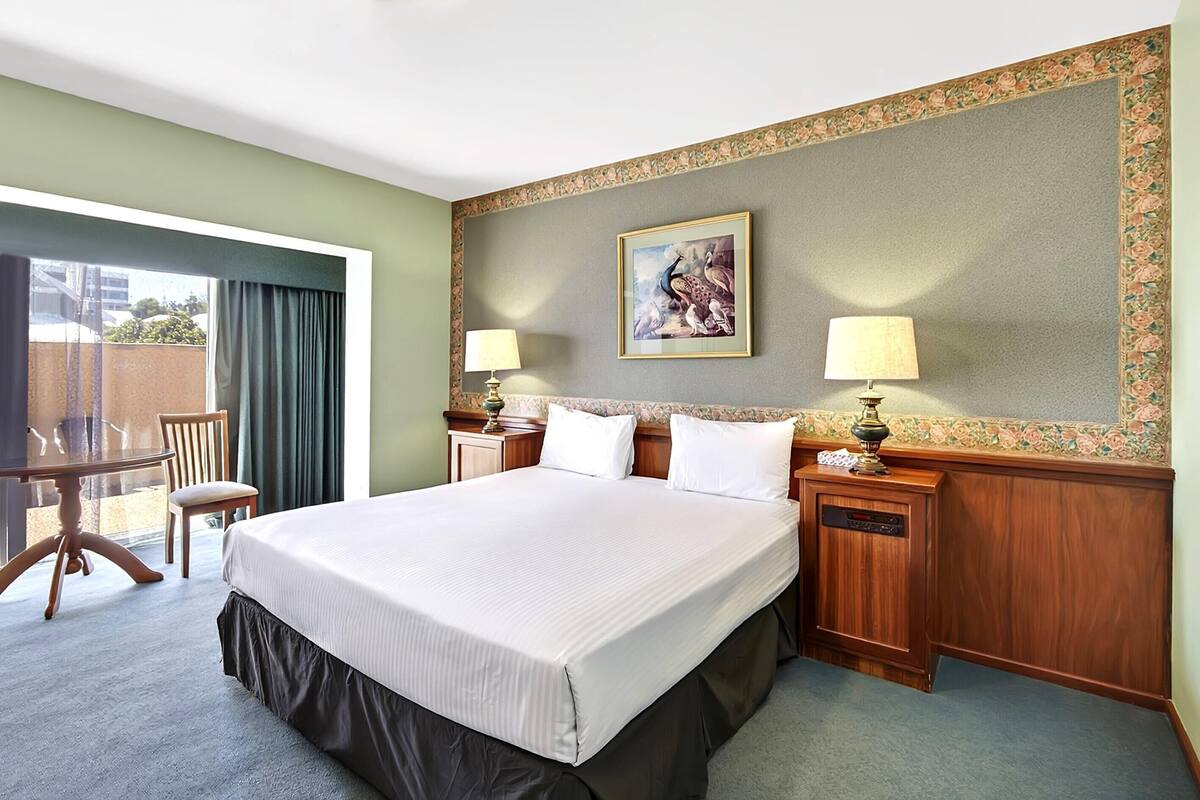 A hotel room with a large bed, two bedside tables with lamps, a chair, and a view of the outdoors.