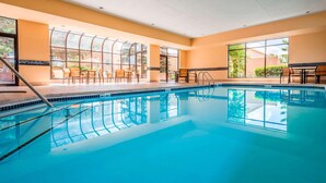Una amplia piscina interior con agua cristalina, rodeada de habitaciones iluminadas por el sol con grandes ventanales y zonas de estar al aire libre.