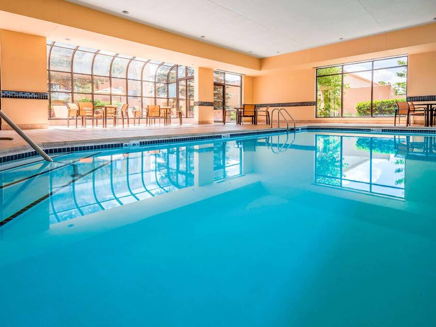 A large indoor swimming pool with clear blue water, surrounded by sunlit rooms with large windows and outdoor seating areas.