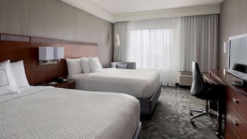 A hotel room with two beds, a desk, a chair, a TV, and a window with curtains.