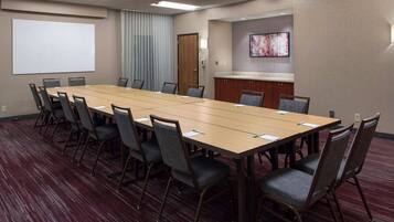 A conference room with a long table, chairs, a whiteboard, and a projector screen.