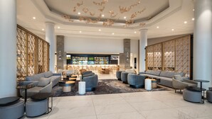 Un vestíbulo amplio con zona de bar, asientos modernos y detalles decorativos en el techo.