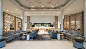Un vestíbulo espacioso de diseño moderno, con una amplia zona de estar con sofás y sillones, un bar al fondo y elementos decorativos en el techo.