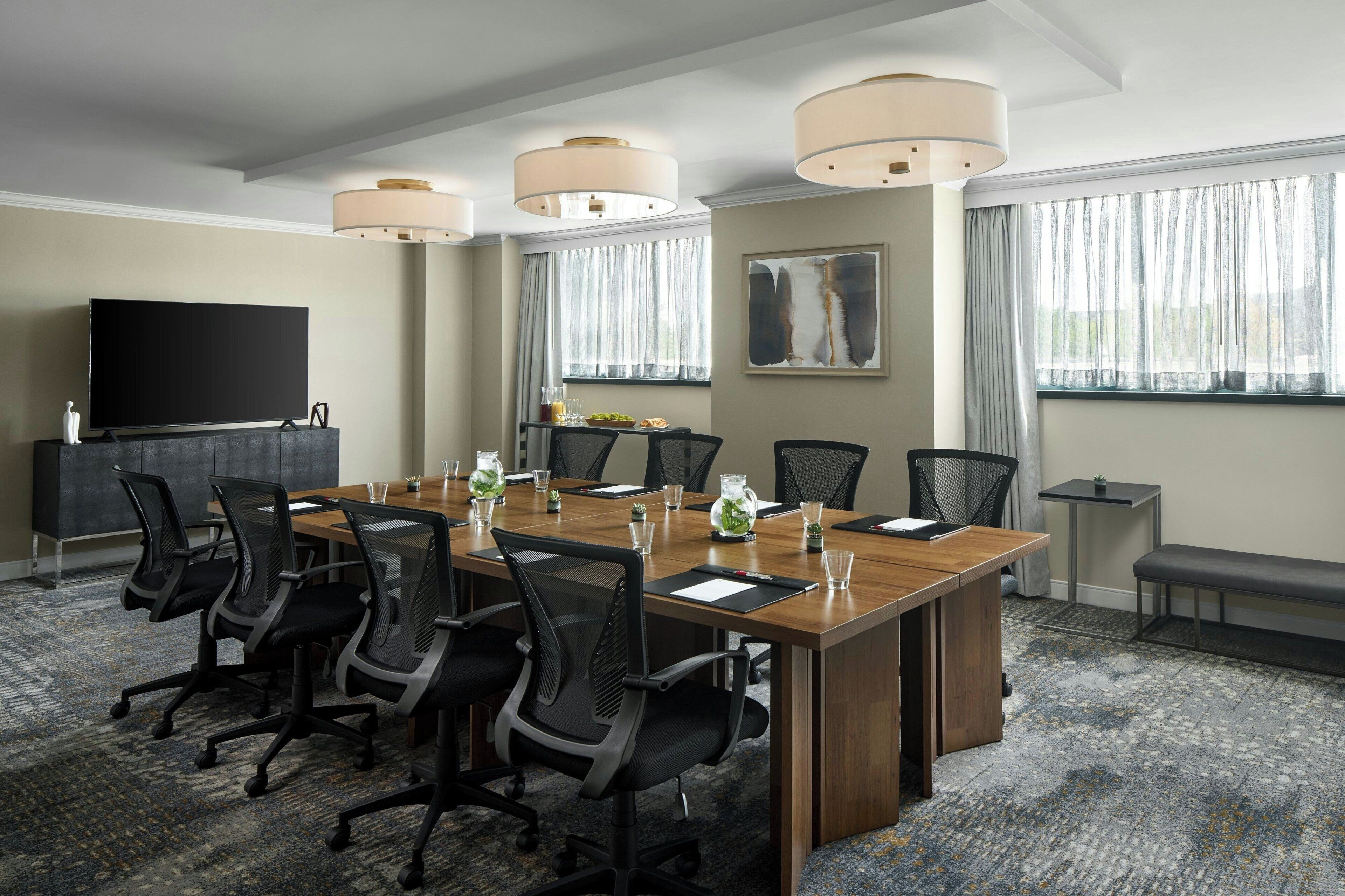 A conference room with a long table, chairs, a television, and large windows with curtains.