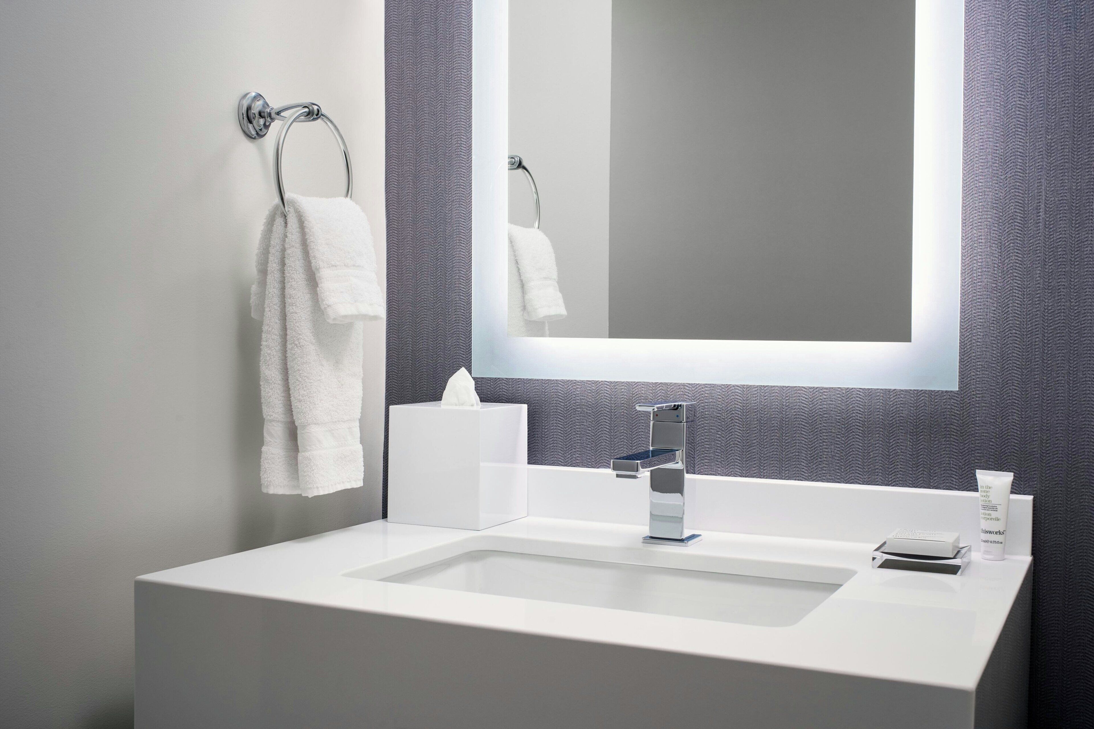 Un baño moderno con un lavamanos blanco, un espejo, un perchero para toallas y una caja de pañuelos.