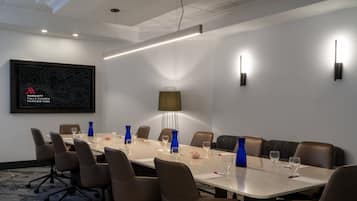 Un salón de conferencias con una larga mesa, sillas marrones y una lámpara moderna.