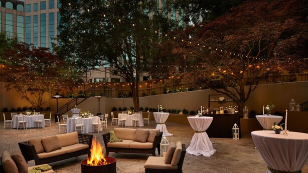 Un patio al aire libre con disposición de mesas y sillas, y luces colgantes.