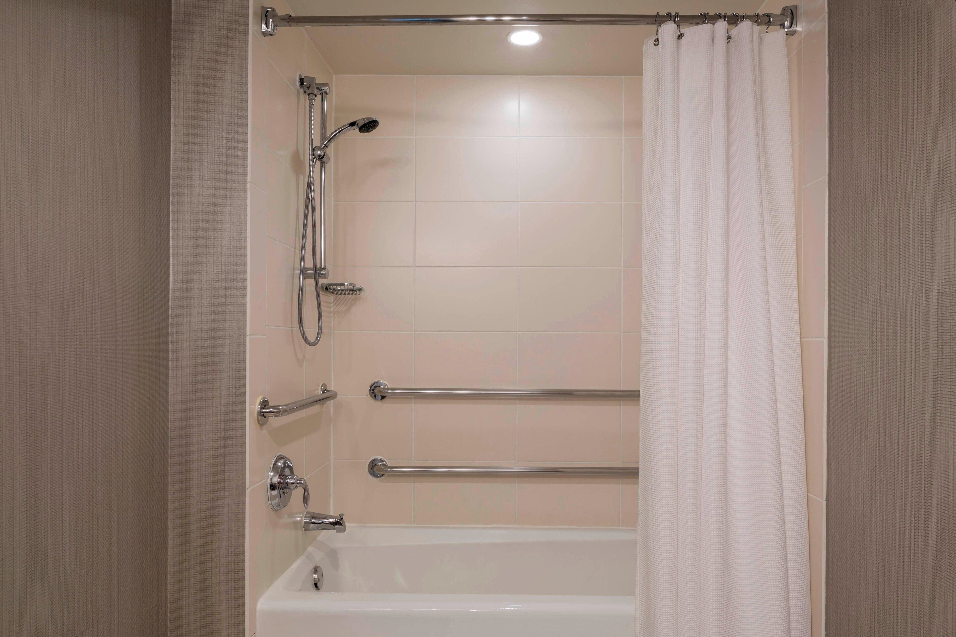 Une salle de bain moderne équipée d’une baignoire, de barres d’appui et d’un pommeau de douche.