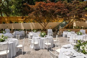 An outdoor dining area with round tables, white chairs, and floral centerpieces. - Falls Church Marriott Fairview Park (Falls Church)