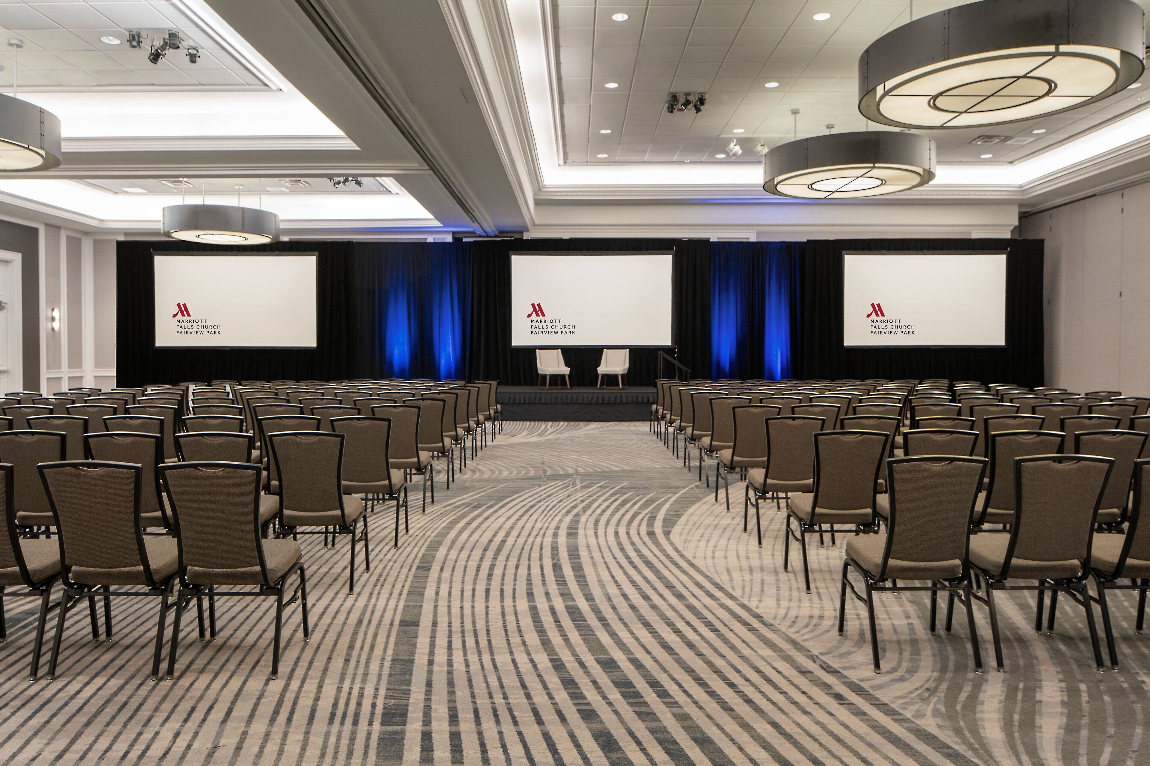 A conference room with rows of chairs, a large screen, and a carpeted floor.