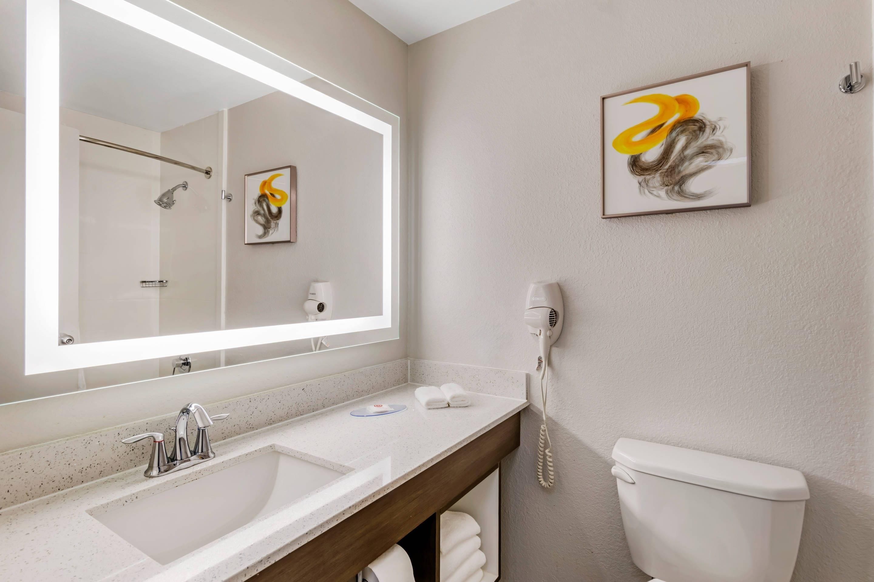 A bathroom with a large mirror, a sink, a toilet, and a hairdryer on the wall.