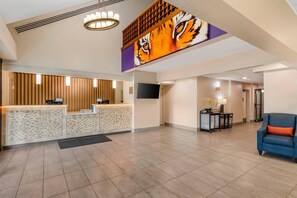 A hotel lobby with a reception desk, a large tiger mural, a TV, and a seating area with a blue sofa.