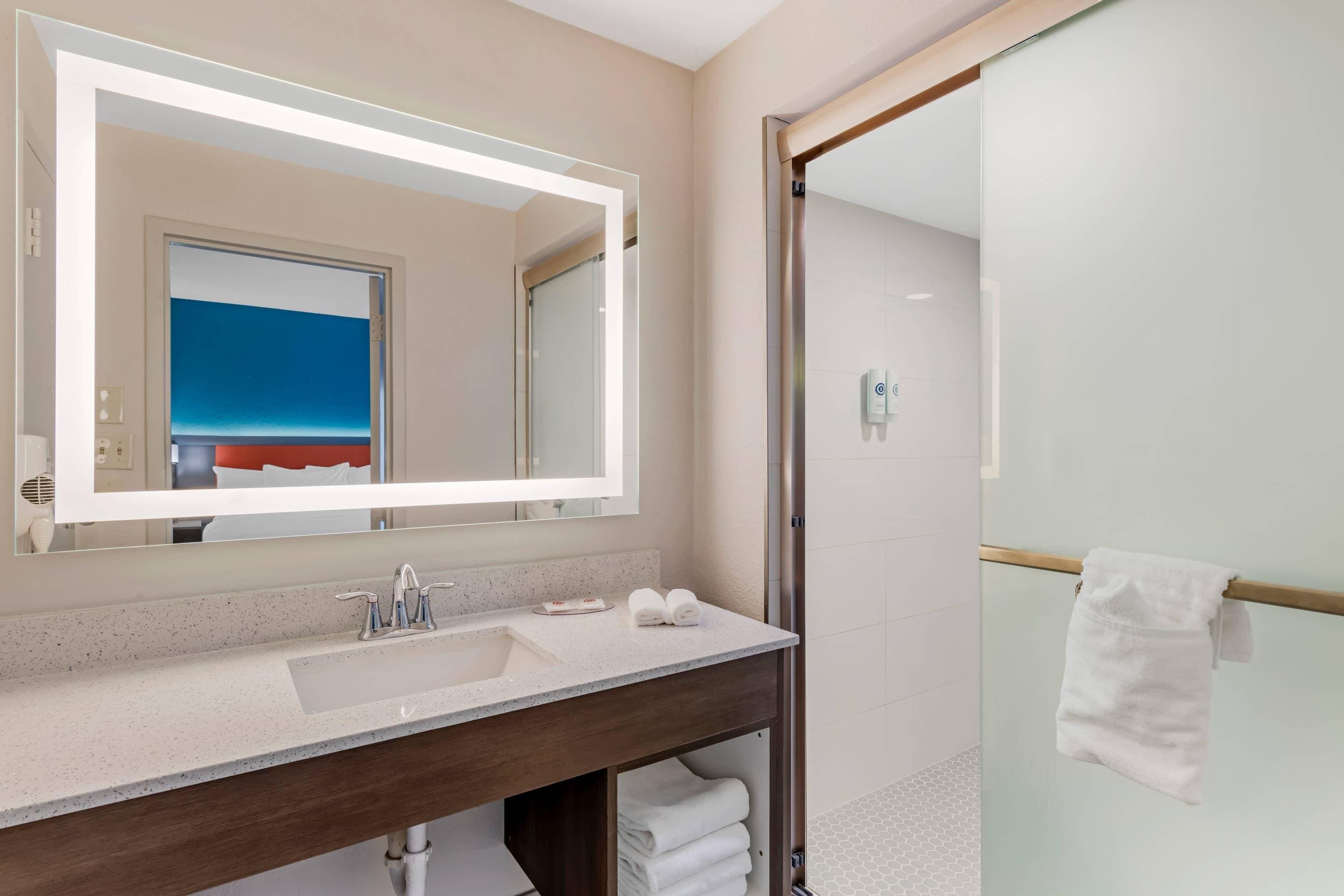 Un baño moderno con un espejo grande, un lavamanos y una cabina de ducha de vidrio.
