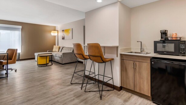 A modern kitchen with a microwave, coffee maker, and bar stools.
