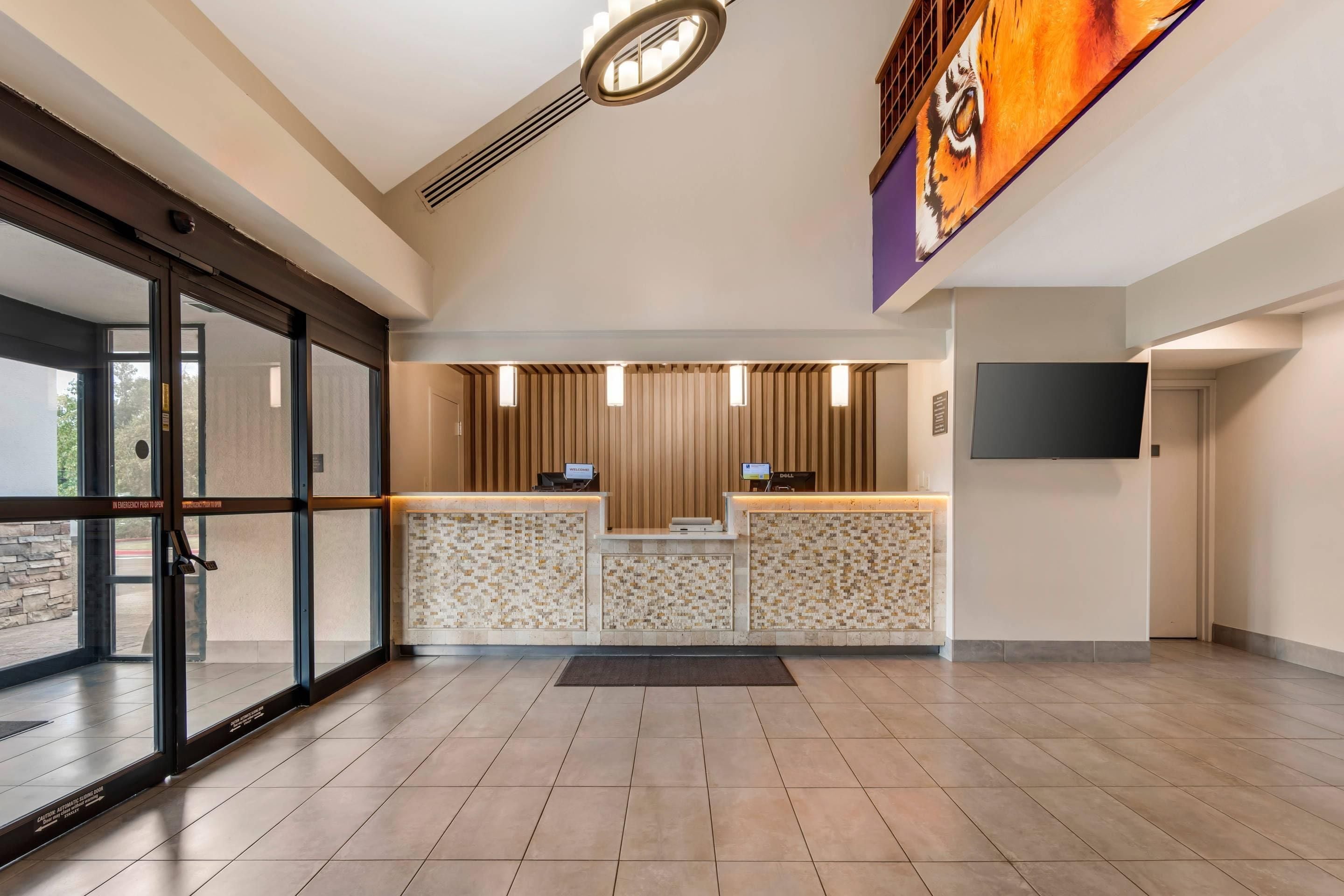 A reception area with a modern design, featuring a reception desk, a flat-screen TV, and a large window with a view of the outdoors.
