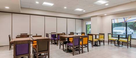A spacious dining area with multiple tables and chairs, a large window with a view of the outside, and a ceiling with recessed lighting.
