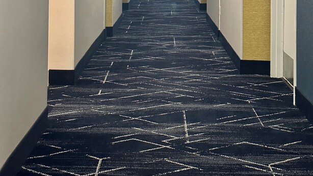 A hotel hallway with a carpeted floor, light-colored walls, and doors on both sides.