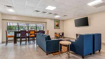 A spacious room with a large window, a flat-screen TV mounted on the wall, and a seating area with sofas and chairs.