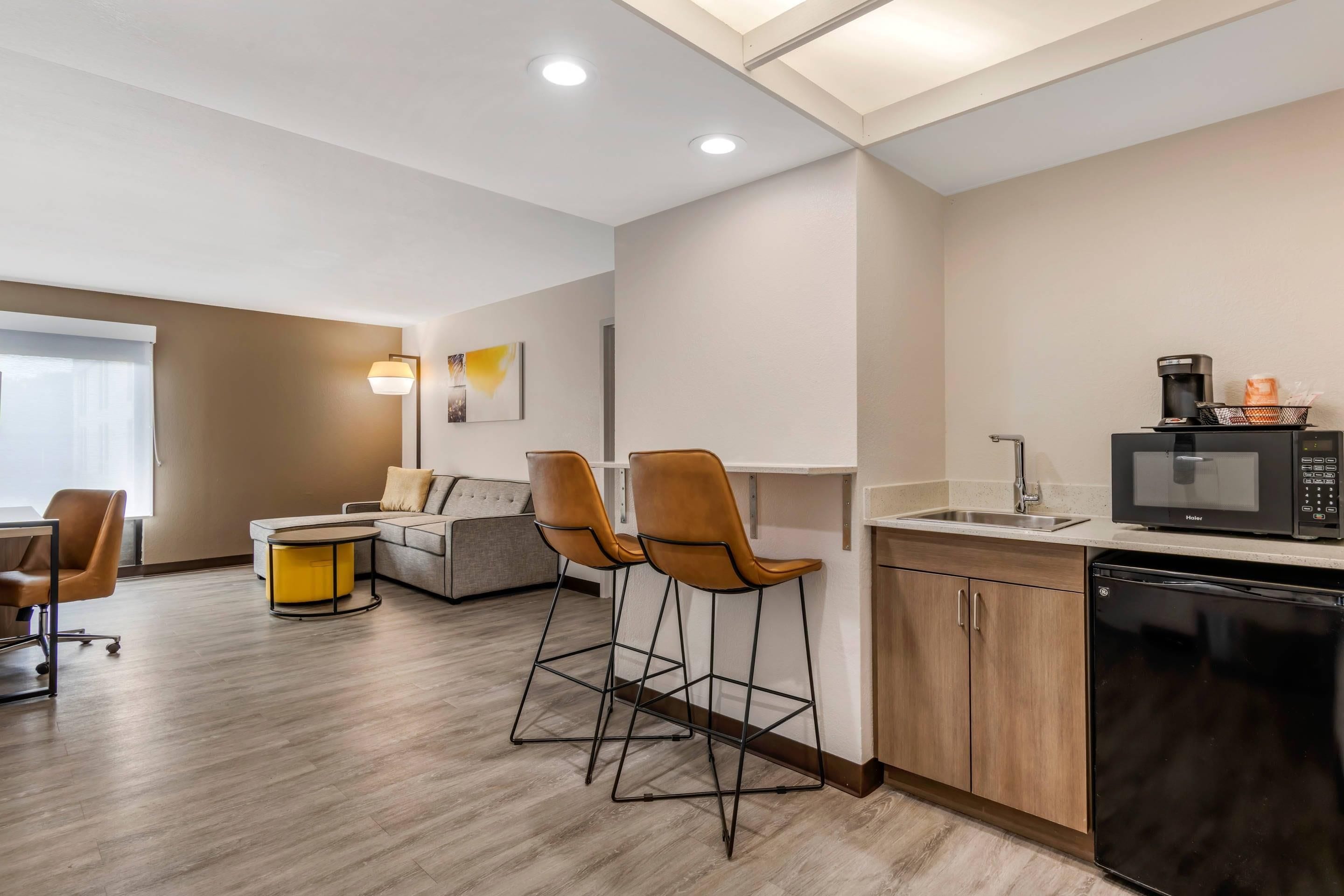 A modern kitchen with a microwave, coffee maker, and bar stools.