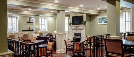 A spacious dining area with wooden tables and chairs, a fireplace, and a television mounted above it.