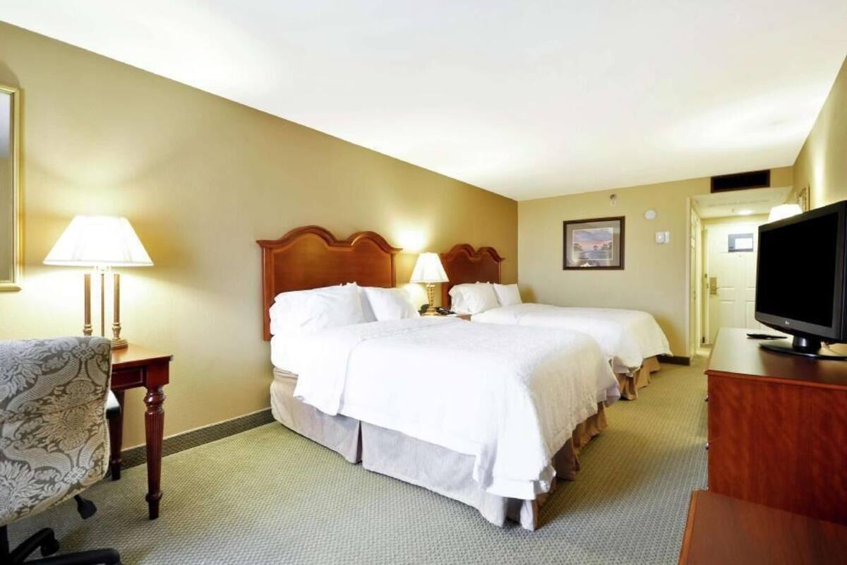 A hotel room with two beds, a television, a desk, and a chair.