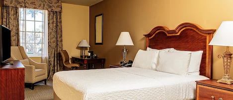 A hotel room with a large bed, a desk with a lamp, a chair, and a television.