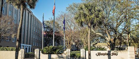 A hotel entrance with a flag, palm trees, and a clear sky.