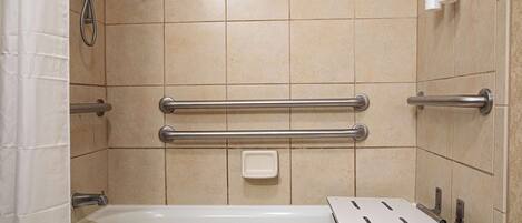 A bathroom with a bathtub, grab bars, a soap dish, and a showerhead.