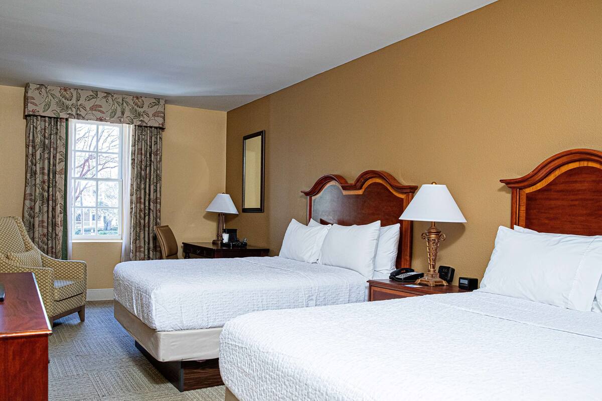 A hotel room with two beds, a desk, a chair, and a window with curtains.