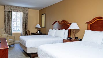 A hotel room with two beds, a desk, a chair, and a window with curtains.