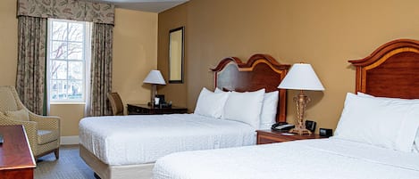 A hotel room with two beds, a desk, a chair, and a window with curtains.