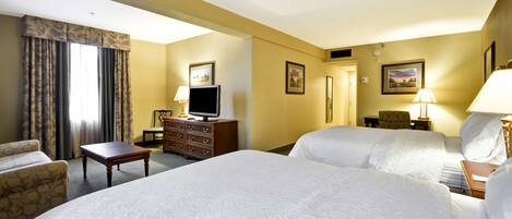 A hotel room with two beds, a desk, a dresser, a television, and two lamps.