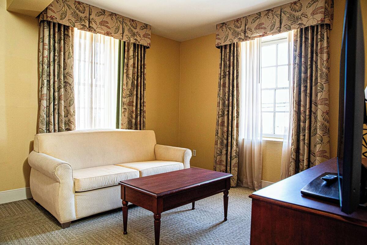 A room with a beige sofa, a wooden coffee table, and a television on a wooden stand.