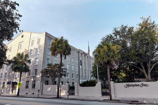 Un edificio grande de varios pisos con una entrada destacada, palmeras y un asta de bandera.