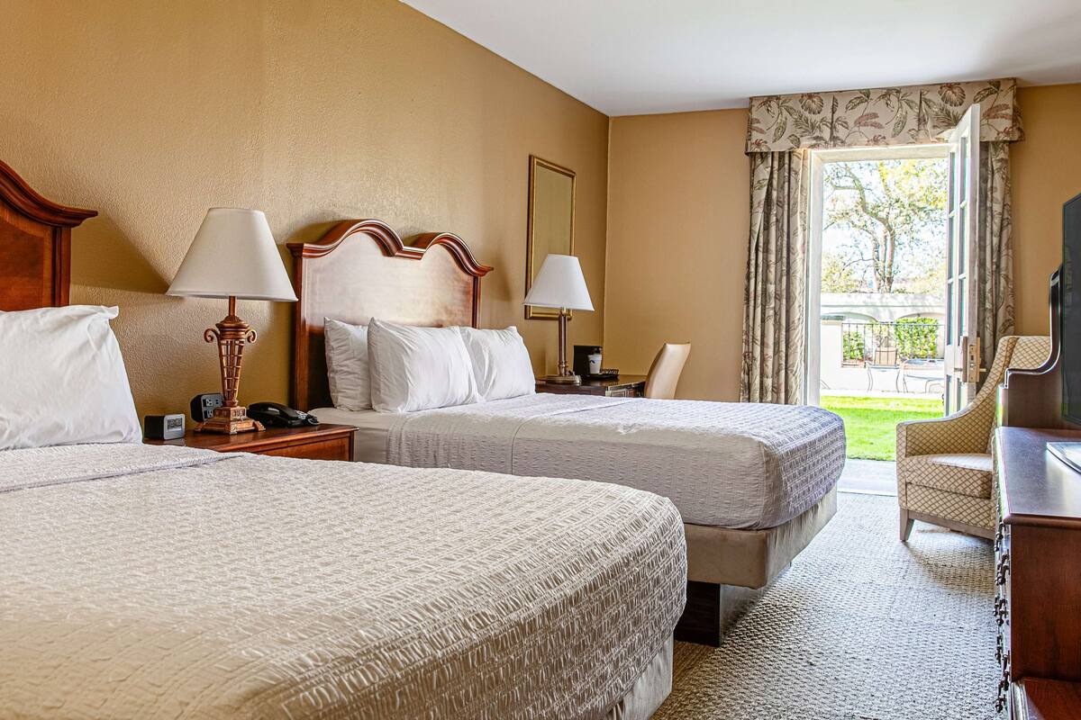A hotel room with two beds, a desk, a chair, and a television.