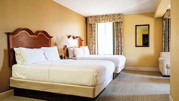 A hotel room with two beds, a sitting area, a large window with curtains, and a mirror on the wall.