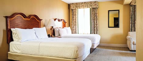 Habitación de hotel con dos camas, una zona de estar, un ventanal grande con cortinas y un espejo en la pared.