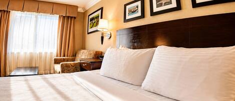 Habitación de hotel con una cama grande, una mesita de noche, una lámpara, una silla y cuadros en la pared.