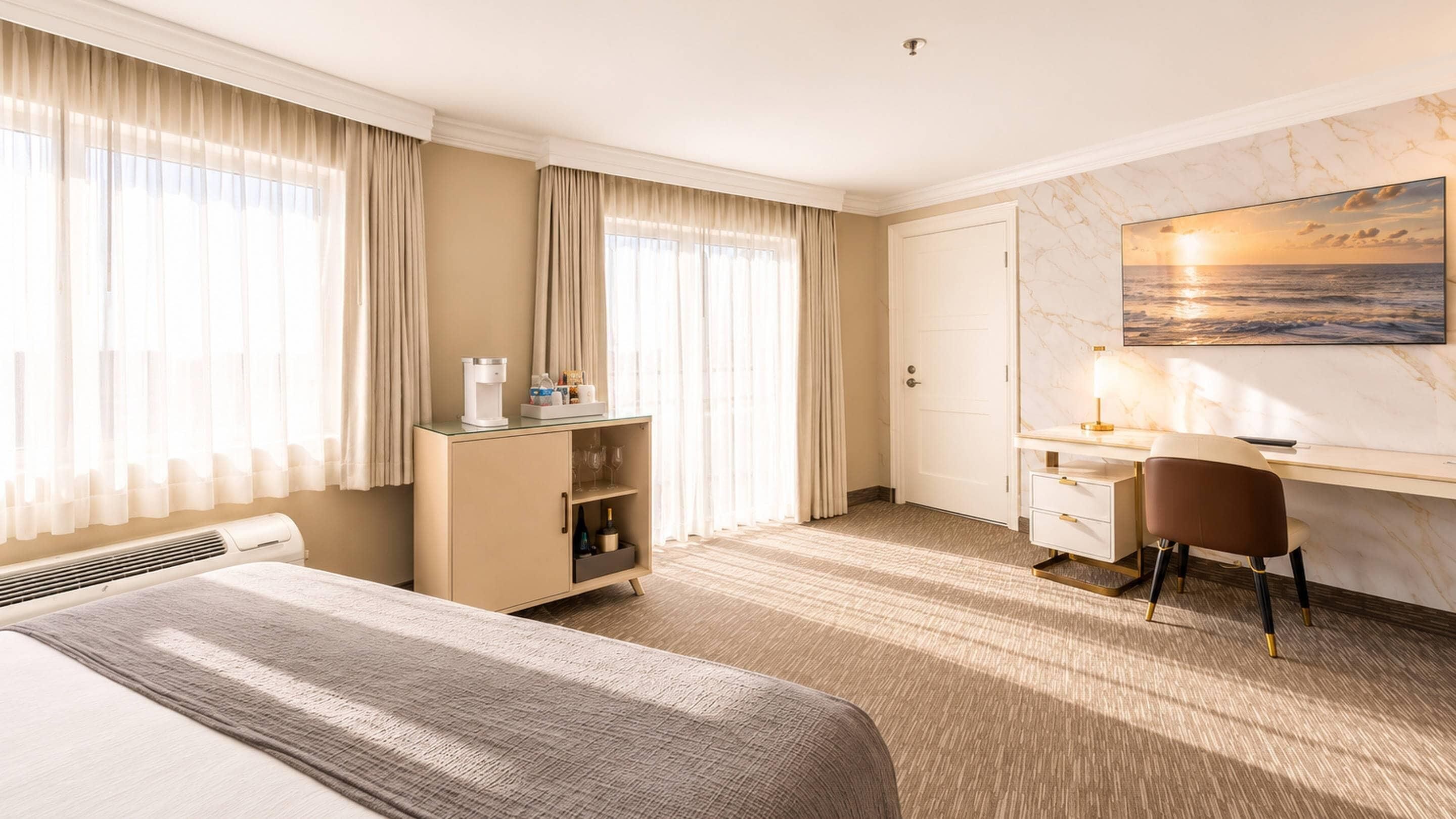 Ein Hotelzimmer mit einem Bett, einem Schreibtisch, einem Sessel, einer Minibar und einem Gemälde, das einen Sonnenuntergang über dem Meer zeigt.